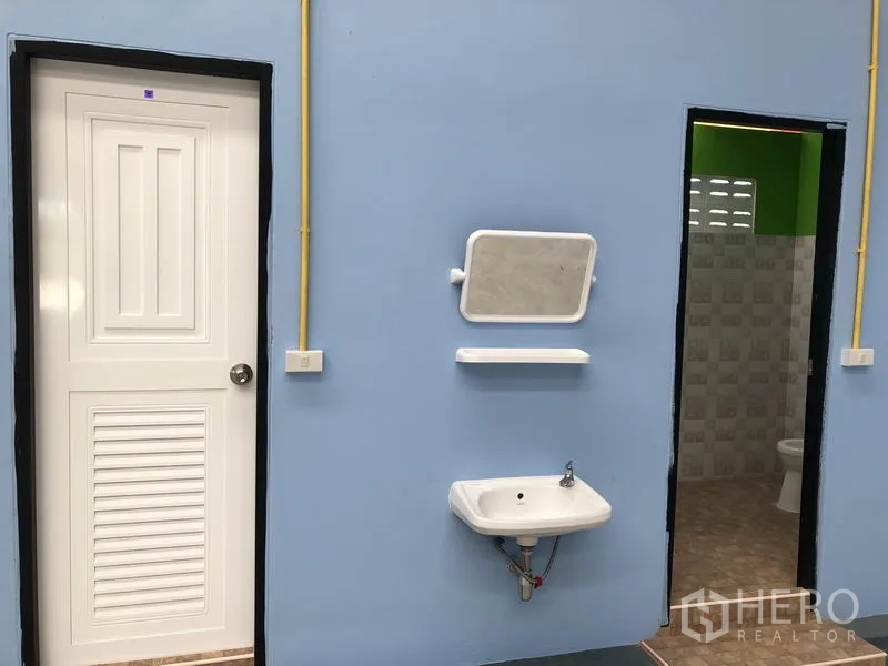 货栈 出租或出售在Sai Noi, Nonthaburi - 卫生间区域，蓝色墙面、白色门，墙挂洗手盆与镜子，瓷砖卫浴。