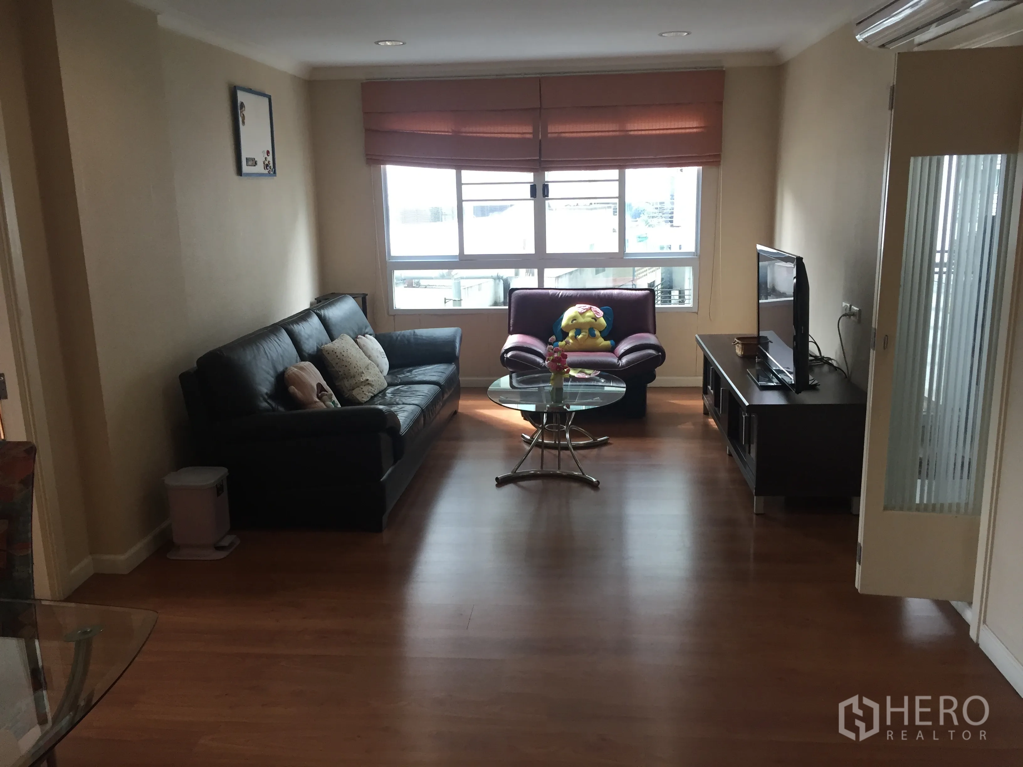 Condominium for rent in Watthana, Bangkok - Bright living room with leather sofa, TV console and glass coffee table on wooden floors, large window providing city views.