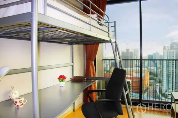 Condominium for rent or sale in Watthana, Bangkok - Loft bed with built‑in study desk facing floor‑to‑ceiling windows and city view.