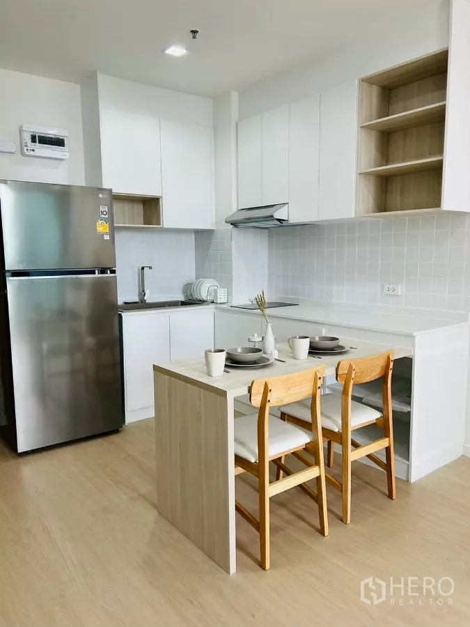公寓 出租在Bang Rak, Bangkok - 现代白色一体式厨房，带岛台餐桌、电磁炉、抽油烟机与不锈钢冰箱。