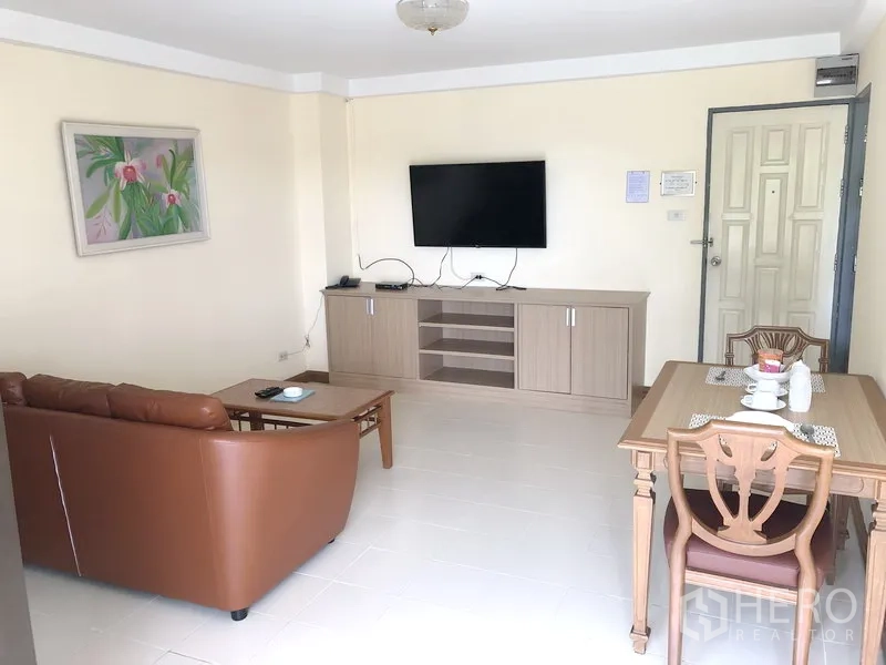 Apartment for rent in Suan Luang, Bangkok - Bright living and dining room with brown sofa, wooden table, TV console and wall-mounted TV near the entrance.