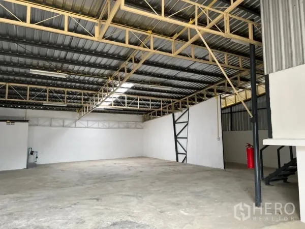 Warehouse for rent in Suan Luang, Bangkok - Spacious warehouse floor with bright lighting, steel beams, and a fire extinguisher near the stairs.