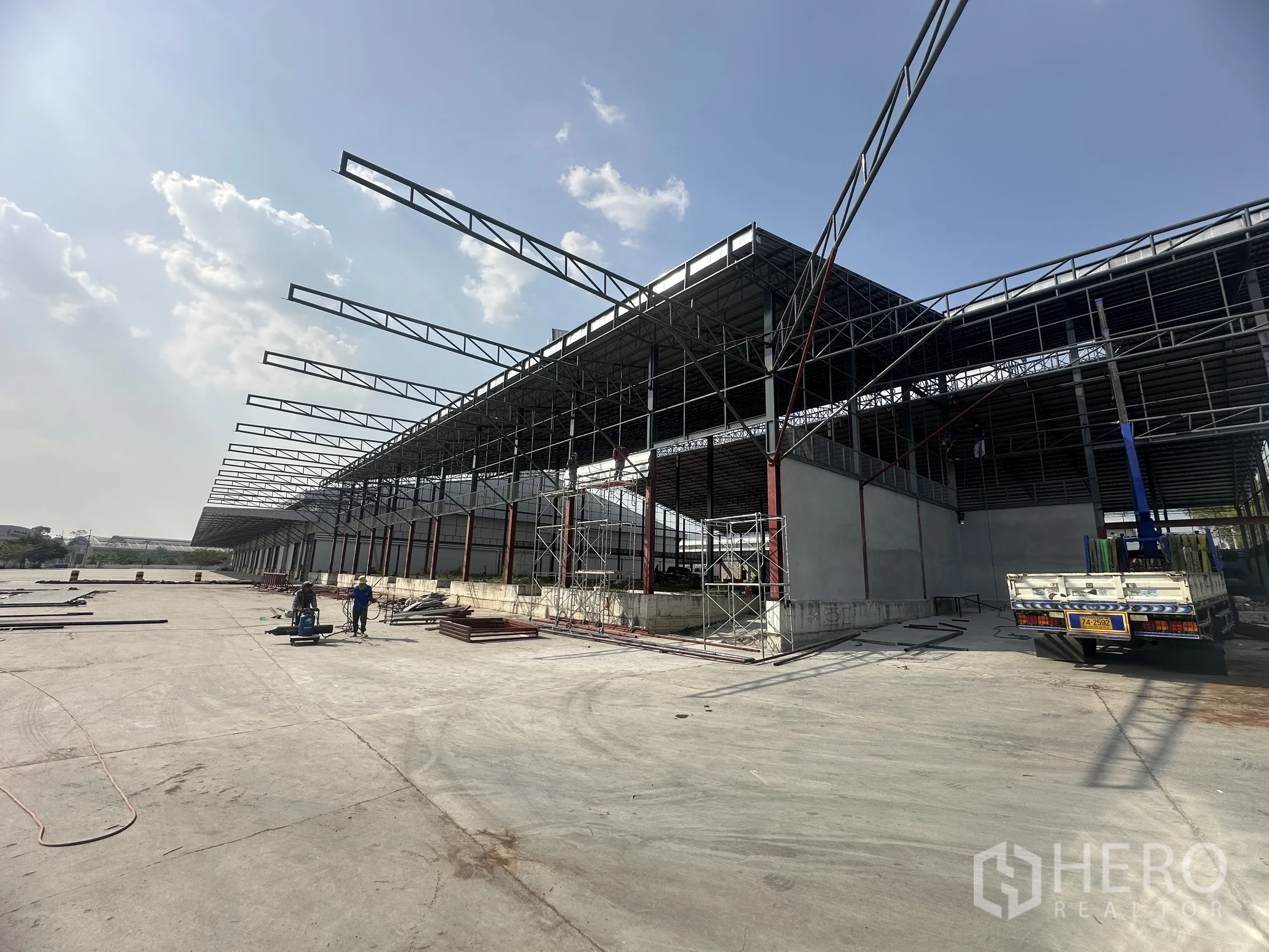 Factory for rent in Si Racha, Chon Buri - Wide logistics yard facing steel-frame factory with raised dock platforms and canopies.