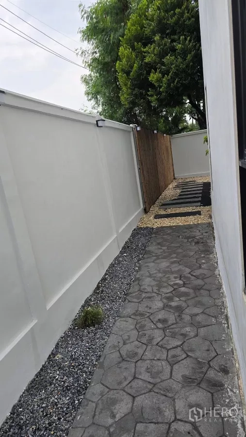 Townhouse for rent or sale in Saphan Sung, Bangkok - Side pathway along white boundary wall leading to the rear garden.