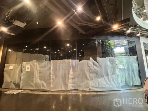 零售空间 出租 - 整面弧形玻璃立面的广角视图，黑色吊顶与射灯，旁侧可见绿植墙。