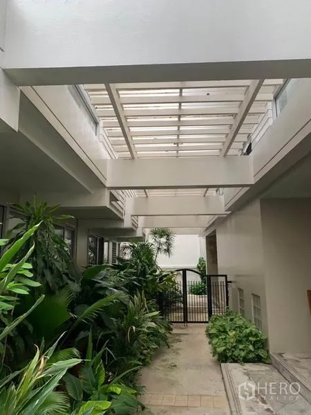 ทาวน์เฮาส์ ให้เช่าในKhlong Toei, Bangkok - โถงทางเดินกึ่งเอาต์ดอร์หลังคาโปร่ง ล้อมด้วยต้นไม้เขียวชอุ่มและประตูเหล็ก