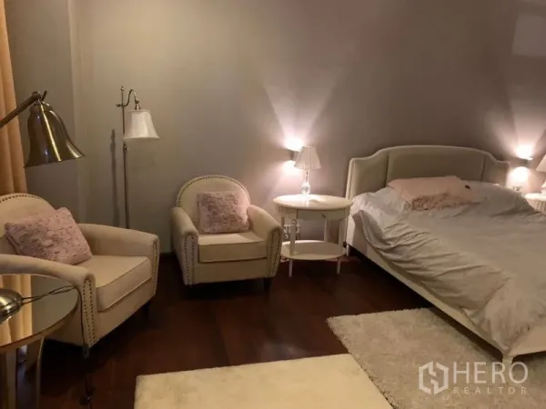 Townhouse for sale in Watthana, Bangkok - Warm master bedroom with upholstered bed, armchairs, side tables and soft lighting on wood floors.