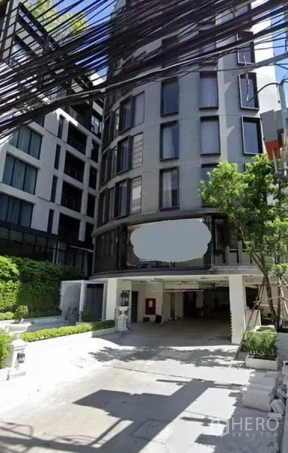 零售空间 出租在Watthana, Bangkok - 现代中高层建筑外立面，弧形玻璃窗、雨棚车道与绿化入口，位于曼谷วัฒนา区。