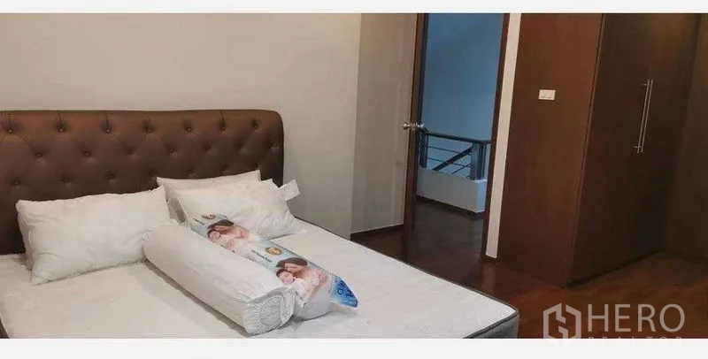 Townhouse for rent in Khlong Toei, Bangkok - Bedroom with an upholstered headboard, mattress, built‑in wardrobe, and wooden flooring.