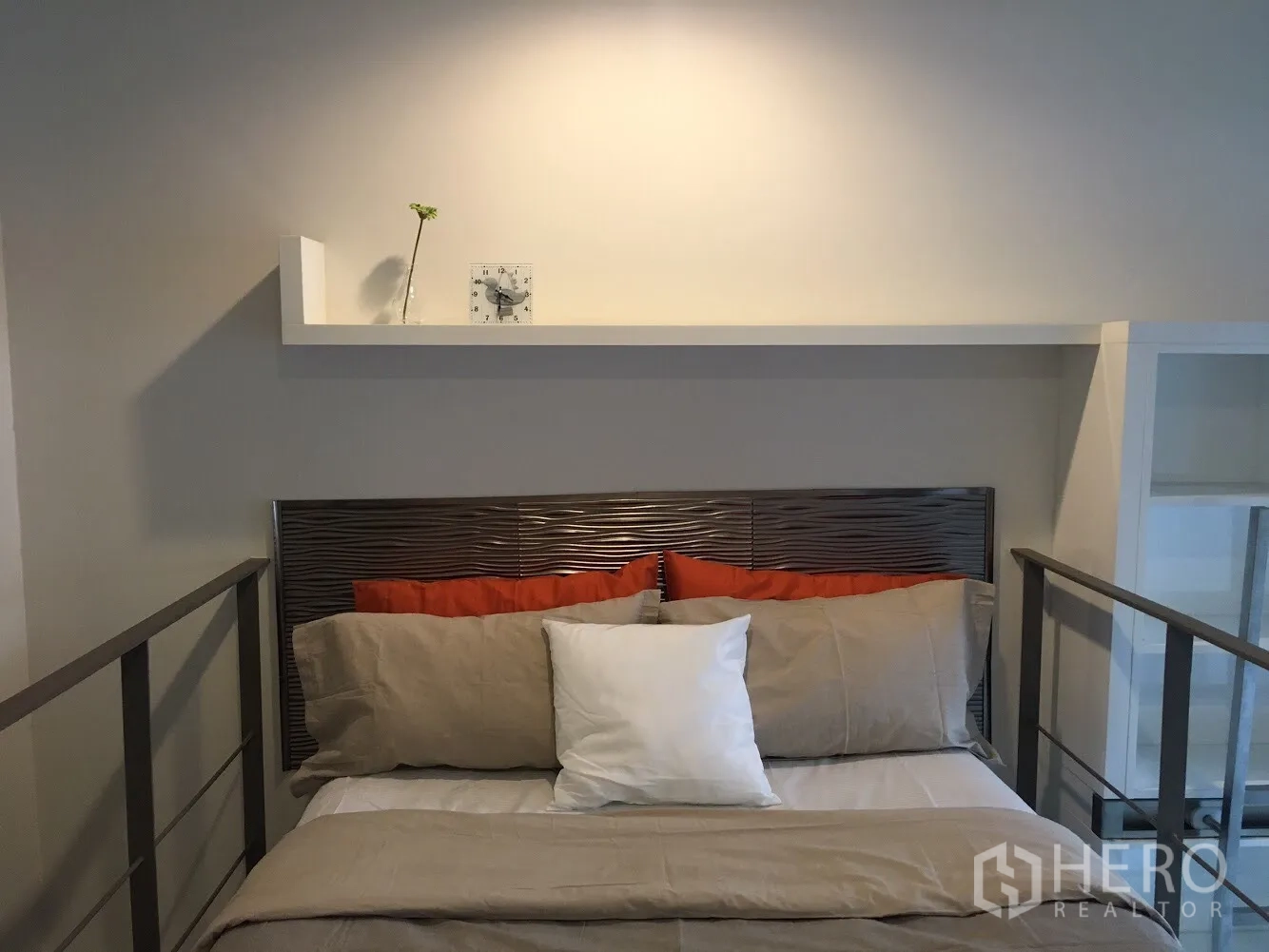คอนโด ให้เช่าในKhlong Toei, Bangkok - ห้องนอนลอฟท์มีชั้นวางและนาฬิกาเหนือหัวเตียง โทนสีอบอุ่นพร้อมราวกันตก