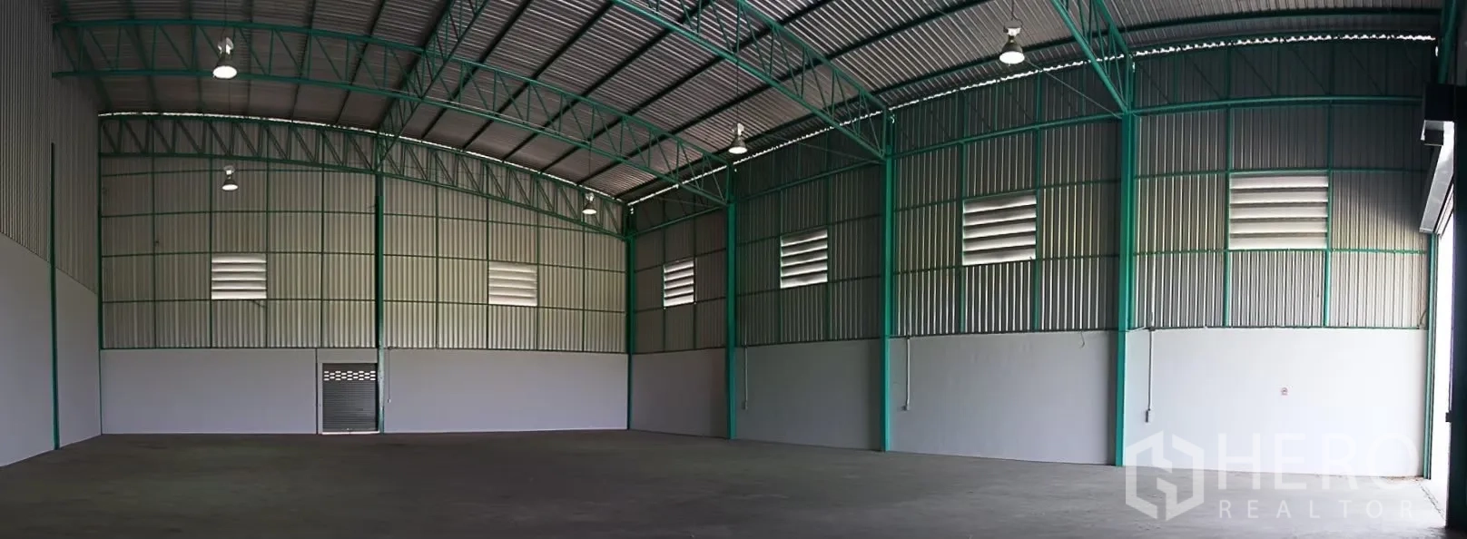 Warehouse for rent in Pathum Thani - Spacious warehouse interior with high arched steel roof, louvered vents, high-bay lighting and smooth concrete floor.