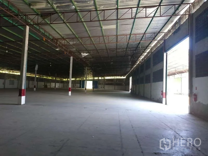 货栈 出租在Mueang Rayong, Rayong - 宽敞仓库内部，侧门开启，混凝土地面。