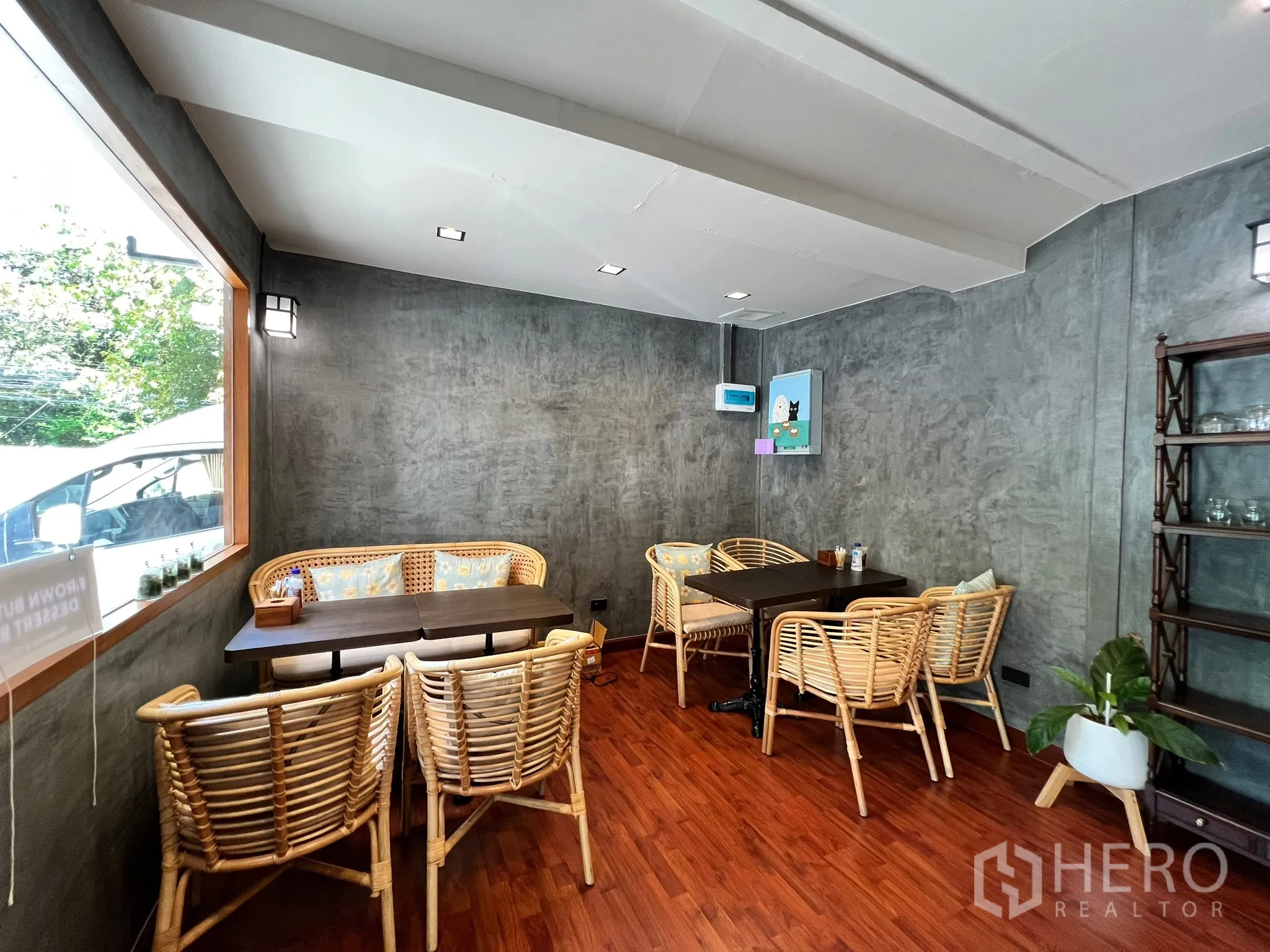 零售空间 出租在Watthana, Bangkok - 临窗座位区，藤椅、混凝土质感墙面、绿植与置物架。