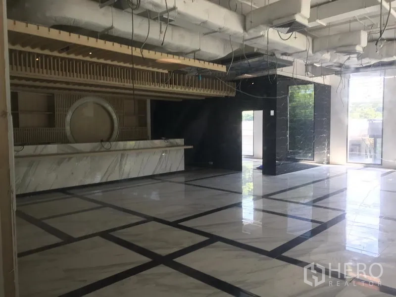 零售空间 出租在Khlong Toei, Bangkok - 宽敞店铺内景，仿大理石地面、挑高天花与外露管线，长条接待台与落地窗采光。