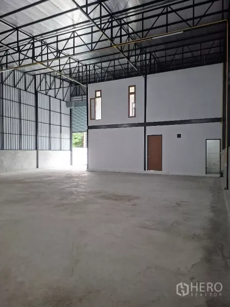 Warehouse for rent in Lam Luk Ka, Pathum Thani - Open warehouse bay with high steel truss roof, partitioned two-storey office block and concrete floor near the loading door.
