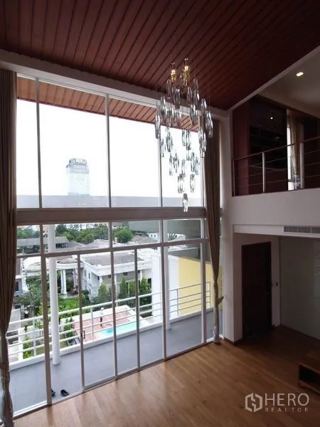 公寓 出租在Chatuchak, Bangkok - 落地窗与水晶吊灯，阳台外可见城市与绿景。