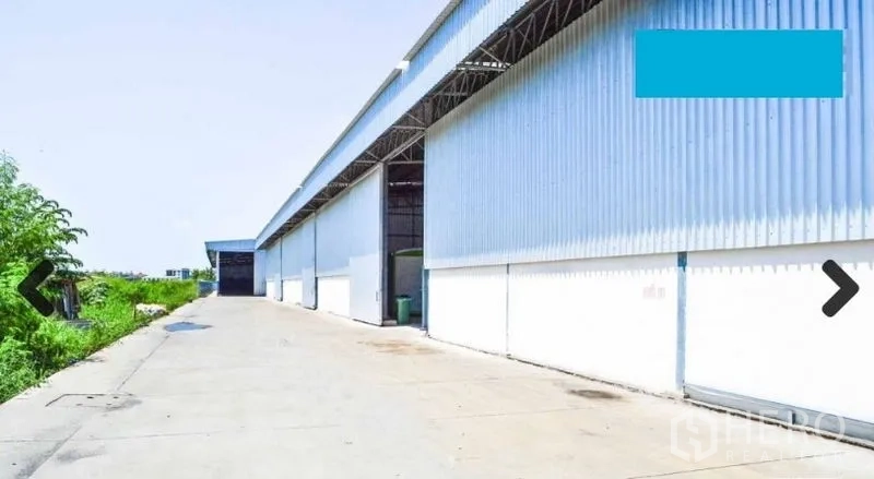 Warehouse for rent in Bang Phli, Samut Prakan - Long corrugated metal warehouse exterior with a wide concrete driveway and sliding bay doors in Bang Phli.