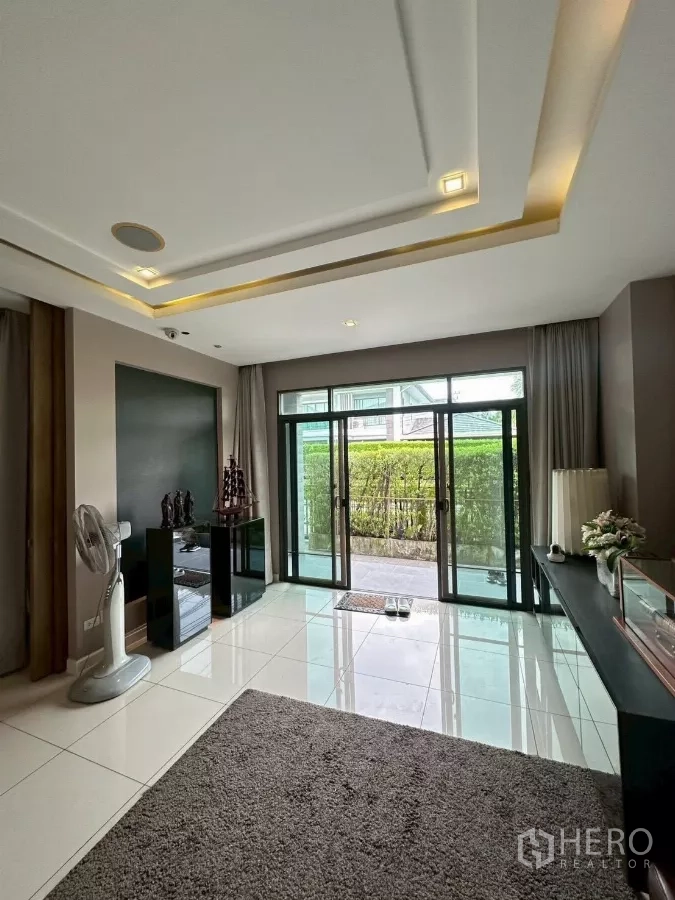 Detached House for sale in Bang Lamung, Chon Buri - Ground-floor sitting area with sliding doors opening to a hedged garden.