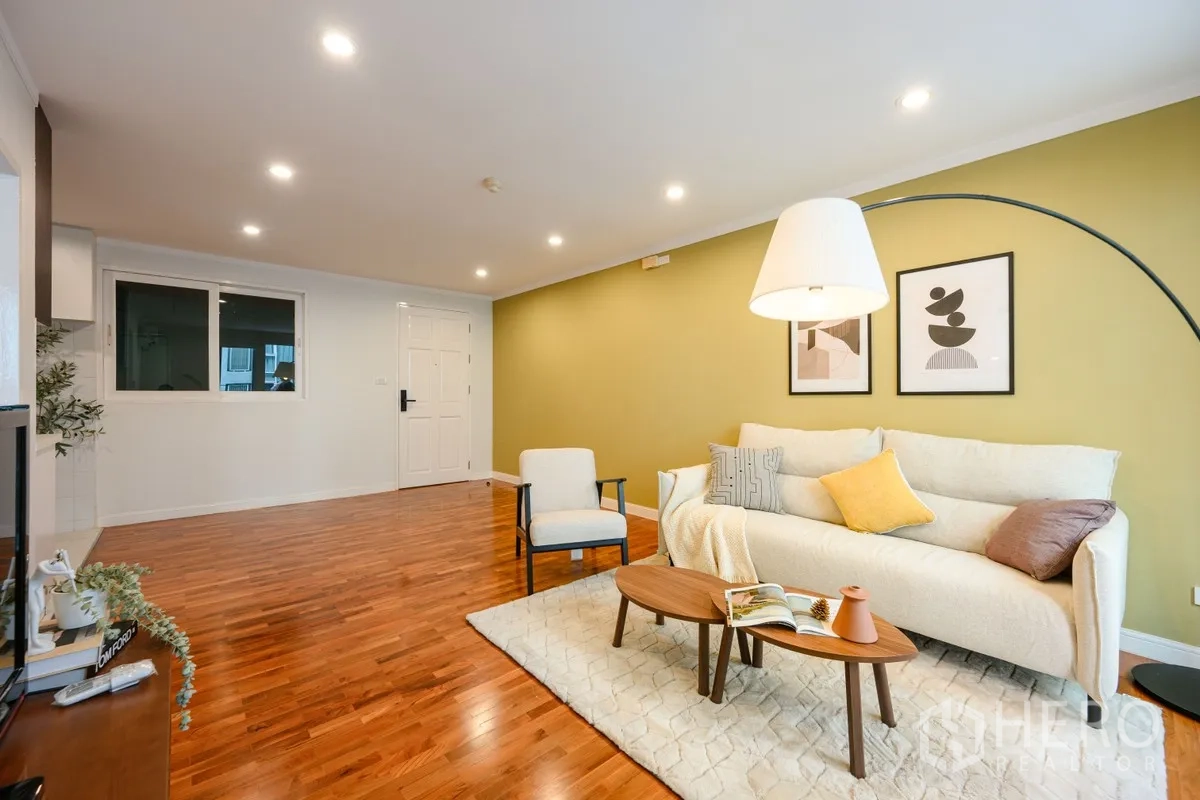 Condominium for sale in Watthana, Bangkok - Spacious lounge with recessed lighting, olive feature wall, rug, and hardwood floors.