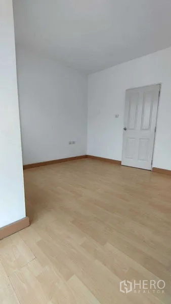 Townhouse for sale in Bang Khen, Bangkok - Empty bedroom featuring light wood flooring and a white paneled door.