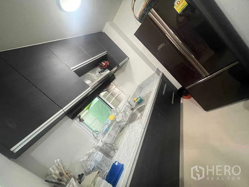 ทาวน์เฮาส์ ให้เช่าในBueng Kum, Bangkok - ครัวรูปตัวไอ พร้อมตู้สีเข้ม เคาน์เตอร์หินอ่อน และตู้เย็นใหญ่