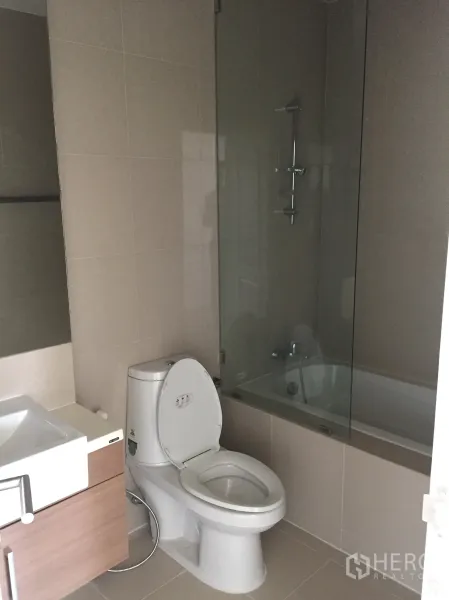 คอนโด ให้เช่าในBangkok - ห้องน้ำสมัยใหม่พร้อมอ่างอาบน้ำ ฉากกั้นอาบน้ำกระจก อ่างล้างหน้า และกระเบื้องโทนอบอุ่น