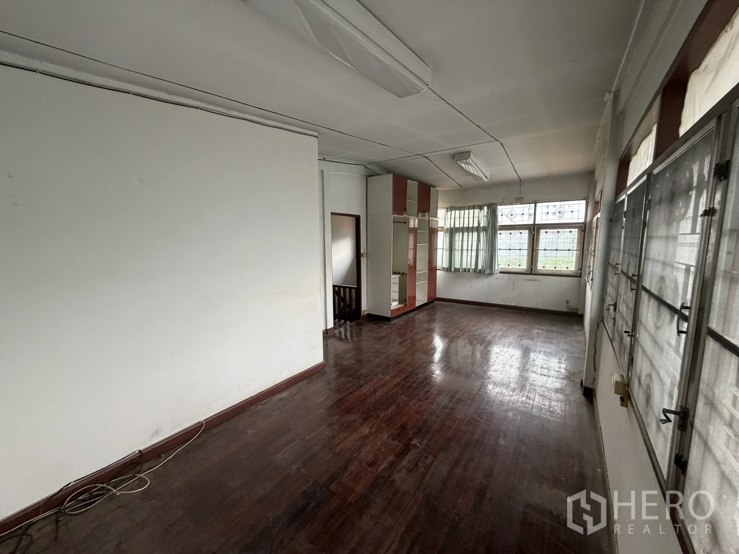 Shophouse for rent in Sathon, Bangkok - Upper floor room with polished wooden flooring and wide windows with grills.