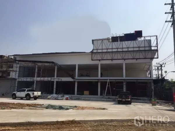 Warehouse for rent in Bang Kapi, Bangkok - Two-storey white warehouse under construction with wide glass bays, scaffolding and a large concrete yard.