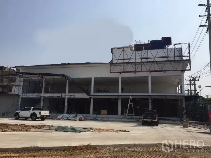 Warehouse for rent in Bang Kapi, Bangkok - Two-storey white warehouse under construction with wide glass bays, scaffolding and a large concrete yard.