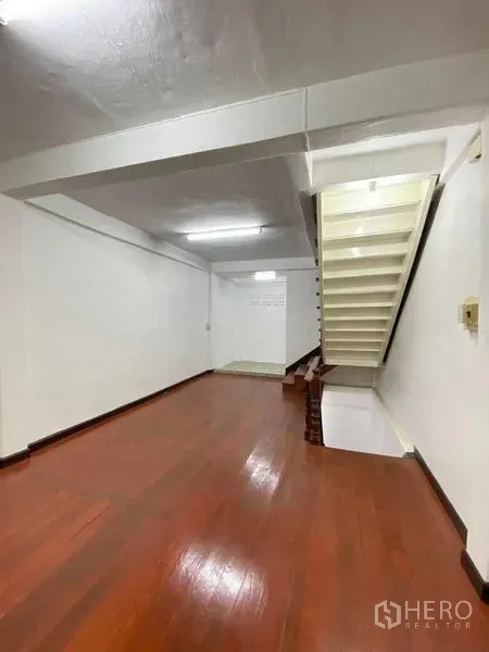 店屋 出售在Phra Khanong, Bangkok - Bang Chak商铺室内，抛光木地板、白色墙面，侧边楼梯通往二层，日光灯照明。