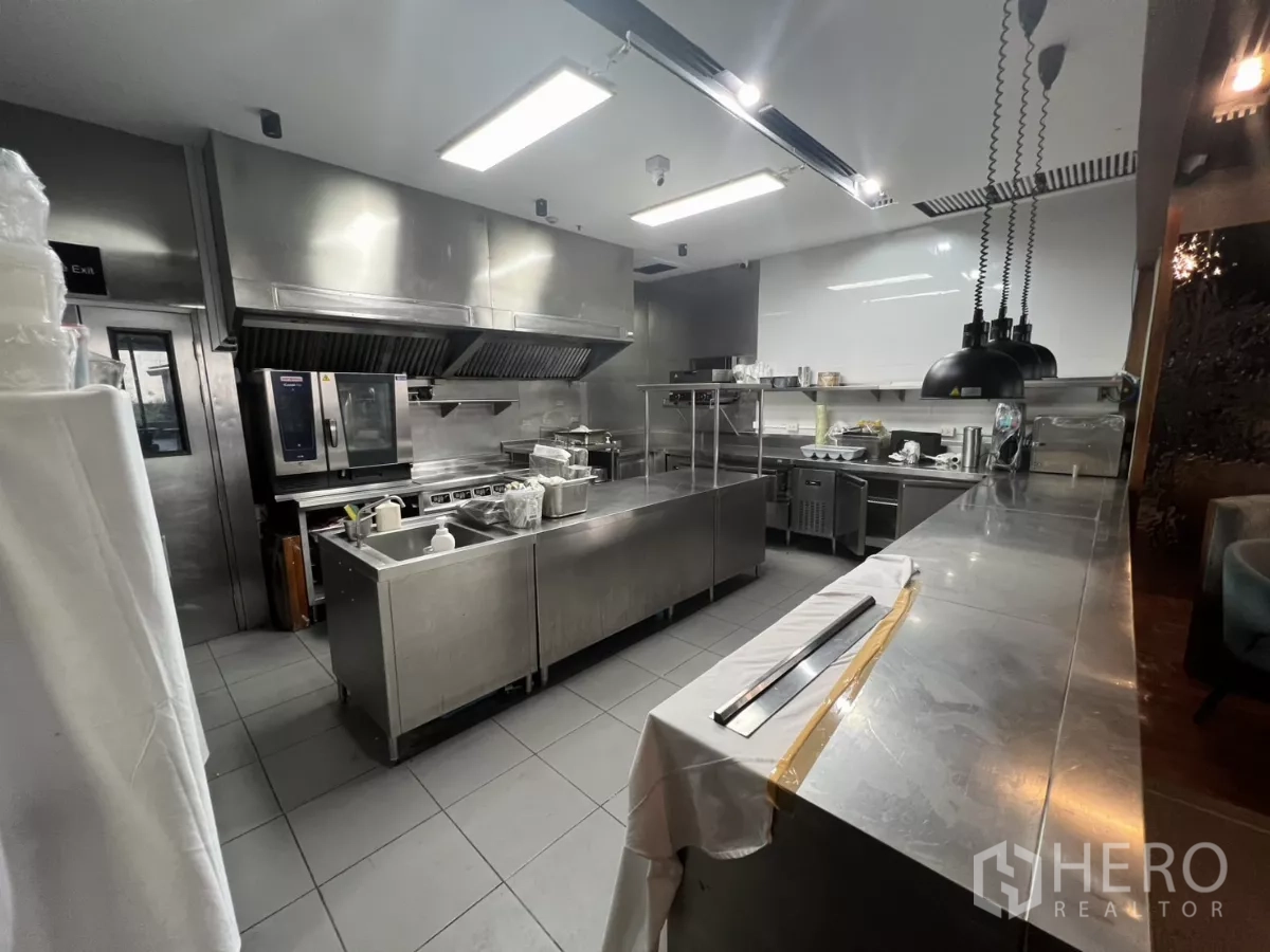 Retail Space for rent - Commercial stainless-steel kitchen with ovens, ventilation hoods and prep stations.