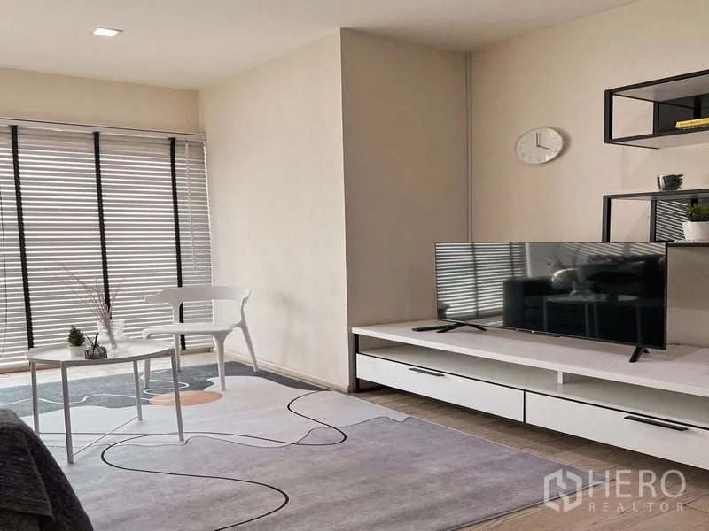 公寓 出租在Khlong Toei, Bangkok - 客厅转角，电视柜、图案地毯、大窗百叶、椅子与边几。