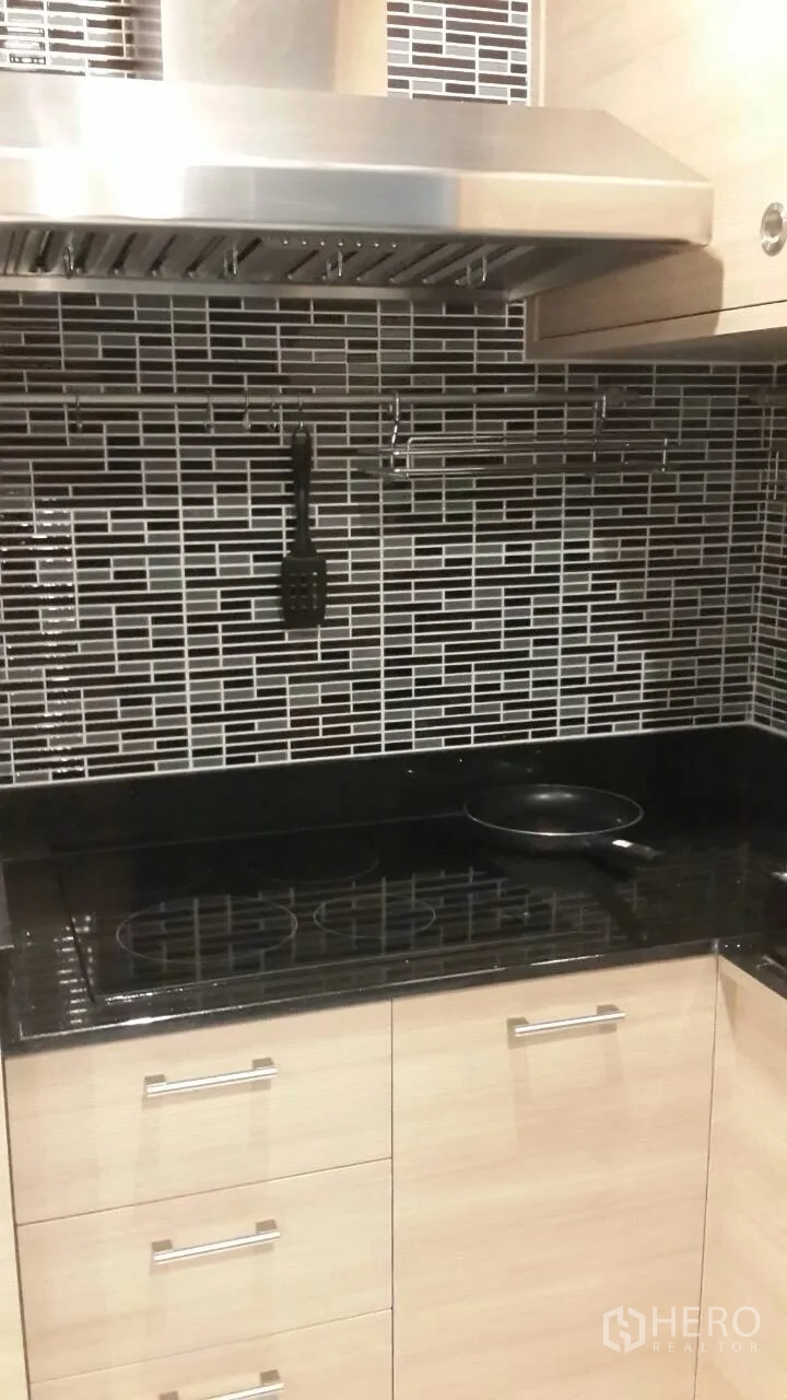 Condominium for rent in Mueang Samut Prakan, Samut Prakan - Modern kitchen close-up with black granite countertop, electric cooktop, stainless range hood, and tile backsplash.