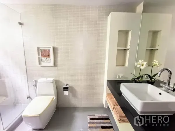 Detached House for rent or sale in Bang Phli, Samut Prakan - Bright bathroom with glass shower, wall niches, square basin on black countertop and toilet.