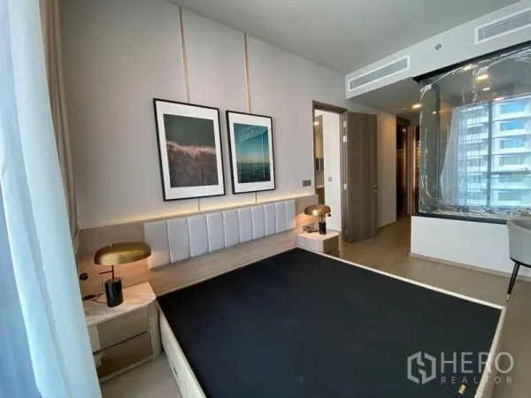 คอนโด ให้เช่าในWatthana, Bangkok - ห้องนอนอบอุ่นพร้อมหัวเตียงบุนวม โคมไฟข้างเตียง หน้าต่างวิวเมือง และผนังกระจกโค้งกั้นห้องน้ำ