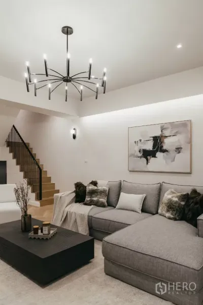 联排别墅 出租在Watthana, Bangkok - 宽敞起居室，灰色转角沙发、楼梯与现代吊灯。