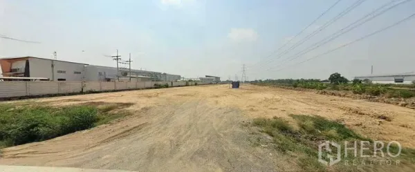 Land for sale in Sai Noi, Nonthaburi - Long rectangular open land bordered by utility lines and nearby industrial buildings.