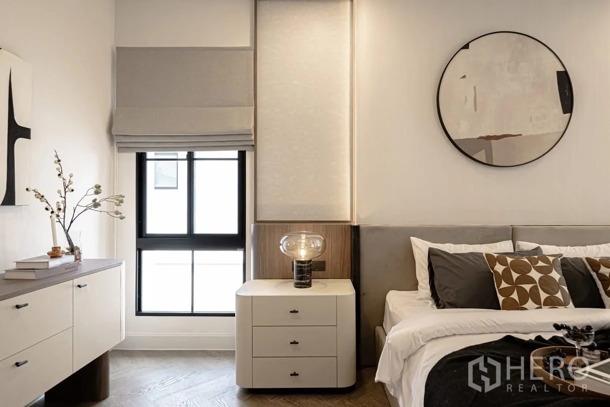 บ้านเดี่ยว for rent in Saphan Sung, Bangkok - โต๊ะหัวเตียงโคมแก้ว ข้างหน้าต่างมู่ลี่โรมัน และตู้ลิ้นชักในห้องนอนสว่าง