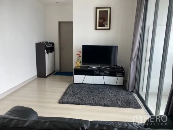 คอนโด ขายในPhra Khanong, Bangkok - ห้องนั่งเล่นสว่างพร้อมชั้นวางทีวี พรม และประตูกระจกเต็มบานเชื่อมระเบียง