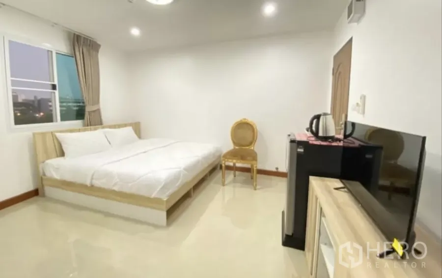 Apartment for sale in Khlong Toei, Bangkok - Large bedroom with glossy tile floor, king bed, TV cabinet, mini fridge and a city-view window.