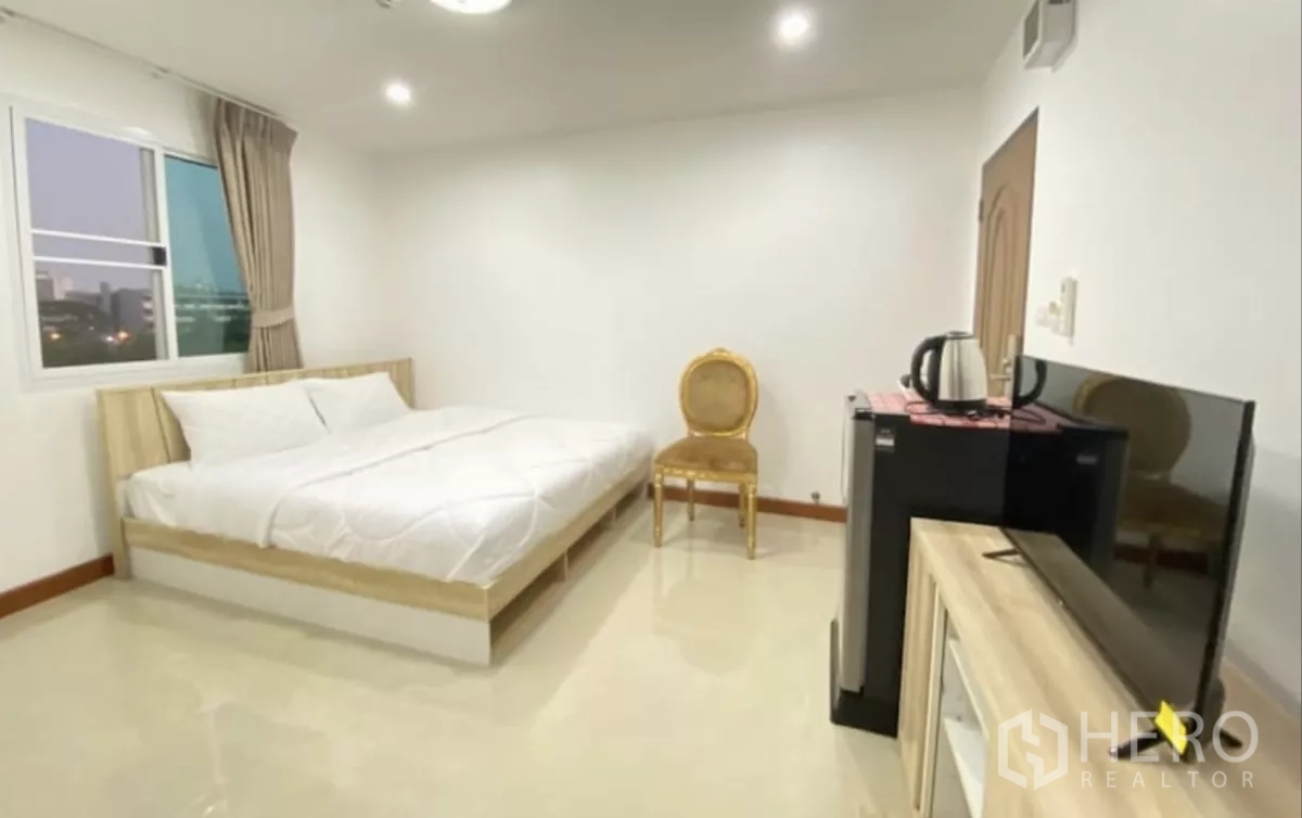 Apartment for sale in Khlong Toei, Bangkok - Large bedroom with glossy tile floor, king bed, TV cabinet, mini fridge and a city-view window.