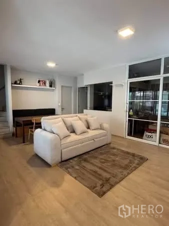 Semi-detached House for rent in Prawet, Bangkok - Living room with sofa on a rug, dining nook, and wood-style flooring.