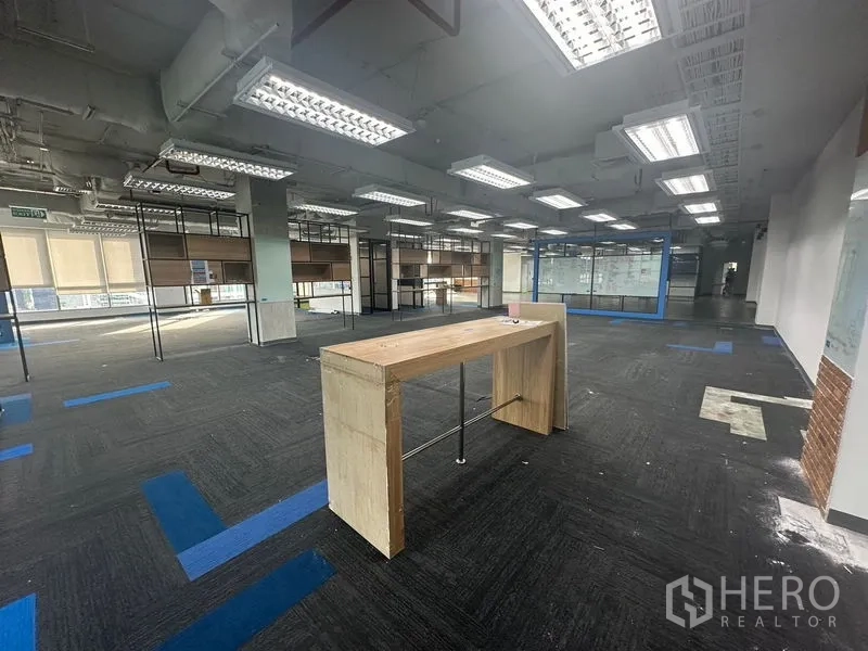 Office Space for rent in Bang Rak, Bangkok - Open-plan office with a standing table, carpet tiles, and a blue-framed meeting room.