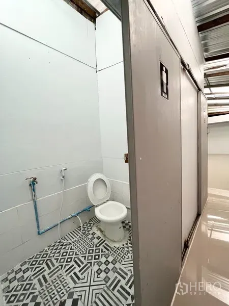 Warehouse for rent in Wang Thonglang, Bangkok - Restroom with toilet, bidet spray, and patterned floor tiles inside the warehouse.