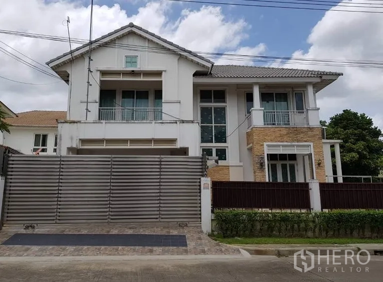 บ้าน ขายในLat Krabang, Bangkok - บ้านเดี่ยวสองชั้นย่านลาดกระบัง กรุงเทพฯ พร้อมประตูเหล็กบานเลื่อน ระเบียง หน้าต่างกระจกสูง และผนังอ磚ตกแต่ง บนลานปูพื้นหน้าบ้าน