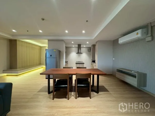 Condominium for rent or sale in Khlong Toei, Bangkok - Dining zone with wooden table, LED-lit feature wall and modern kitchen.