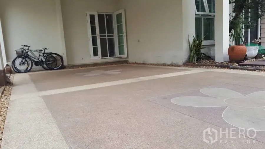 บ้าน ขายในMueang Nonthaburi, Nonthaburi - ที่จอดรถในร่ม พื้นคอนกรีตลายดอกไม้ จักรยาน และประตูกระจกเข้าสู่ตัวบ้าน