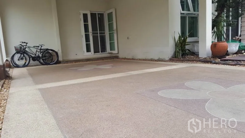 บ้าน ขายในMueang Nonthaburi, Nonthaburi - ที่จอดรถในร่ม พื้นคอนกรีตลายดอกไม้ จักรยาน และประตูกระจกเข้าสู่ตัวบ้าน