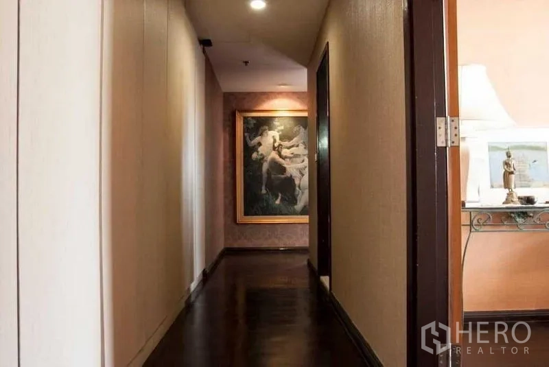 Condominium for rent in Watthana, Bangkok - Hallway with dark wood floors, neutral walls, recessed lights and framed artwork at the end.