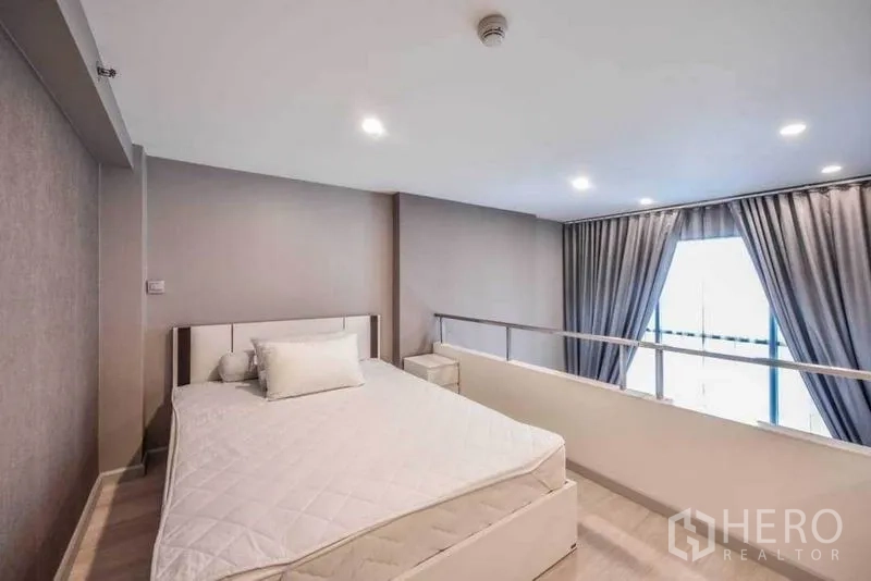 Condominium for rent in Sathon, Bangkok - Mezzanine bedroom with natural light from double-height windows and grey blackout curtains.